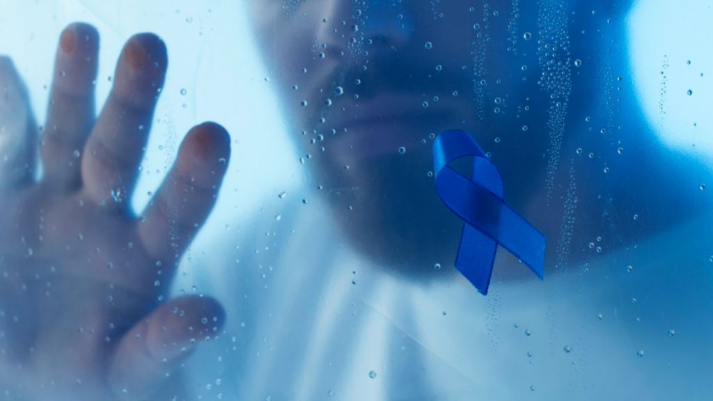 Homem escorado no vidro, com um laço azul, falando sobre a importância da prevenção no novembro azul