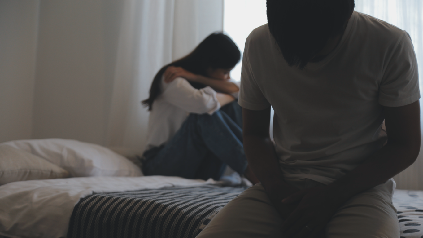 Casal em um quarto à meia luz, insatisfeitos com a disfunção erétil e a doença de peyronie